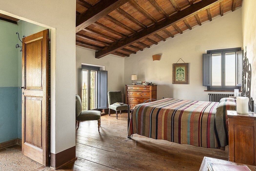Een slaapkamer met een houten plafond, een bed met een gestreept dekbedovertrek, een dressoir, een stoel en een raam met uitzicht.