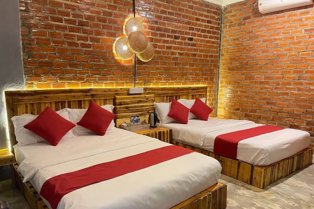 Une chambre d’hôtel avec deux lits en bois, des oreillers rouges, un mur en briques et un luminaire moderne.
