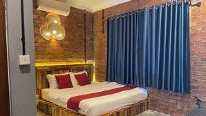 A room with a brick wall, a bed with white and red bedding, a blue curtain, and a hanging light fixture.