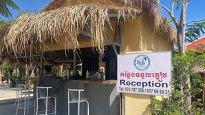 A reception area with a thatched roof, a signboard with contact information, and two white metal chairs.