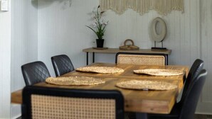 A dining area with a wooden table, black chairs, macrame wall hanging, and hanging plants. - Island Oasis Near Waterfalls and Hilo`s Markets (Hilo)