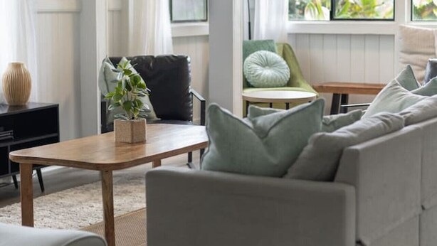 A modern living room with a grey sofa, a wooden coffee table, and a black chair. There is a window with curtains and a view of greenery outside. - Island Oasis Near Waterfalls and Hilo`s Markets (Hilo)