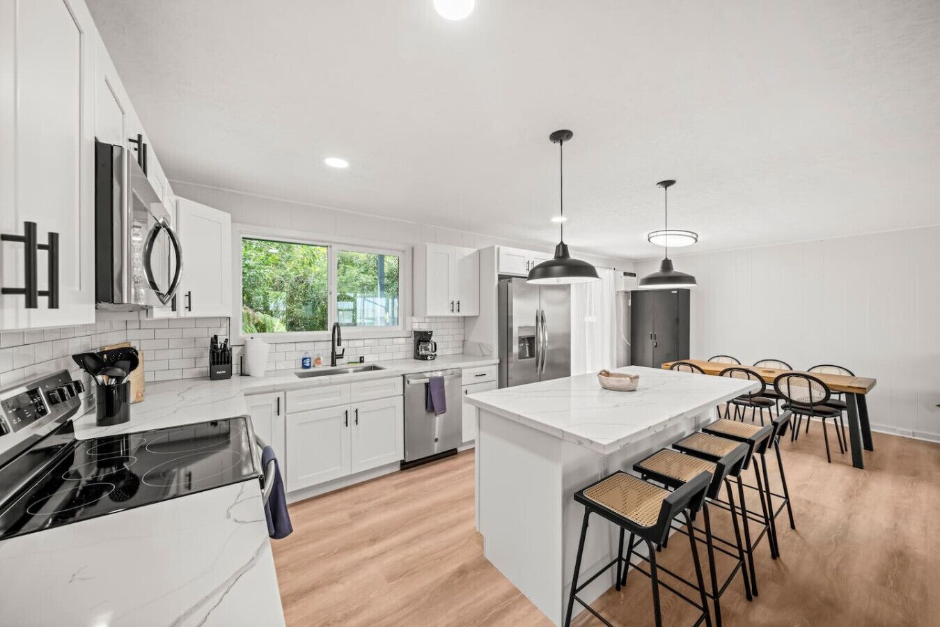 A modern kitchen with white cabinetry, a central island with bar stools, stainless steel appliances, and pendant lighting.