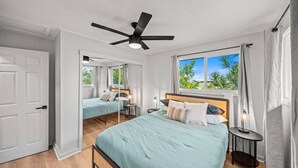 A bedroom with a bed, a nightstand, a ceiling fan, and a window with a view of greenery.