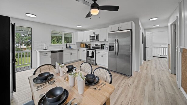 A modern kitchen with white cabinets, stainless steel appliances, and a dining area with a wooden table and chairs. - Garden Oasis, Walkable to Downtown Hilo (Hilo)