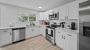 A modern kitchen with white cabinets, stainless steel appliances, and a window providing natural light. - Garden Oasis, Walkable to Downtown Hilo (Hilo)