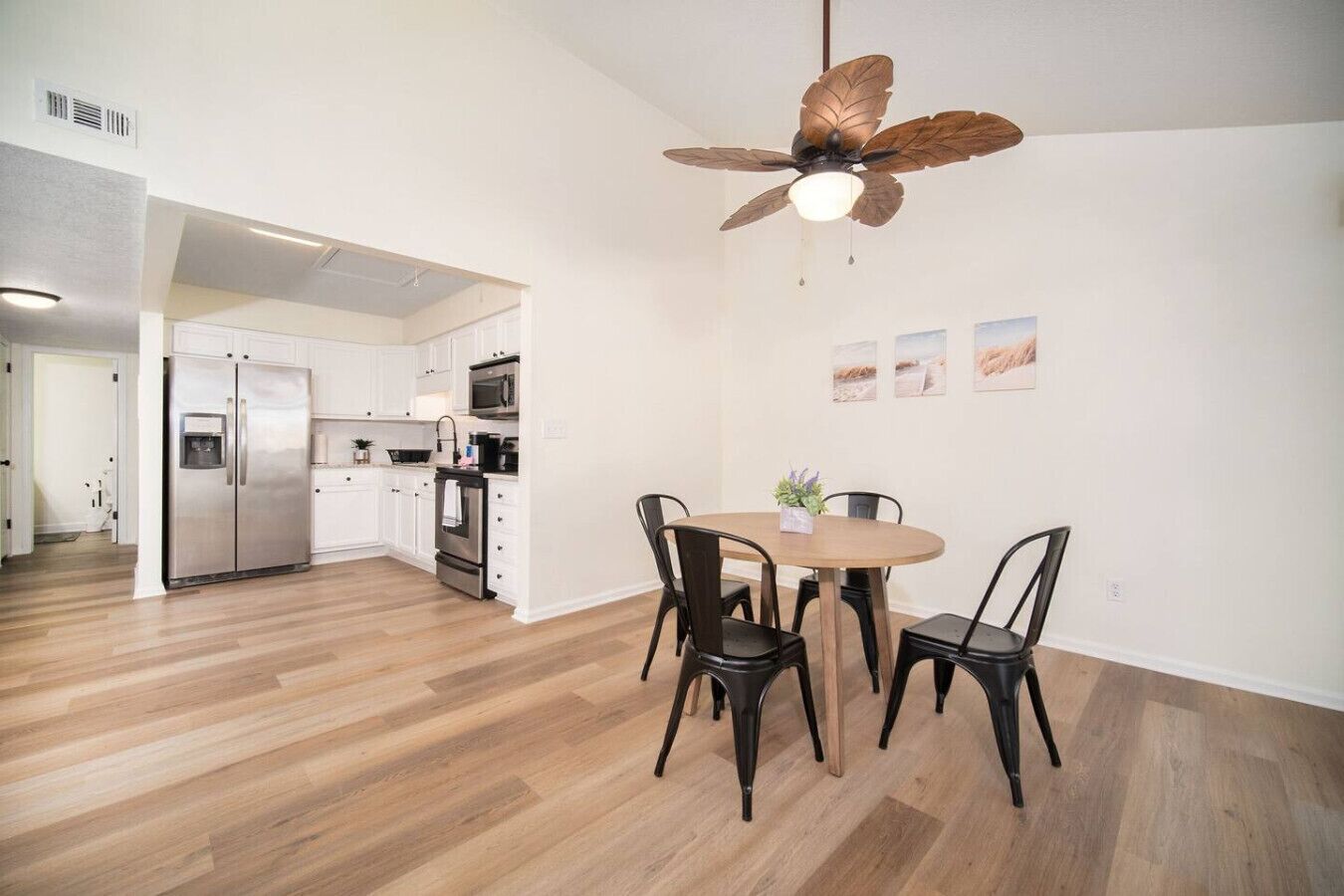 A modern kitchen with white cabinets, stainless steel appliances, and a wooden dining table with black chairs.