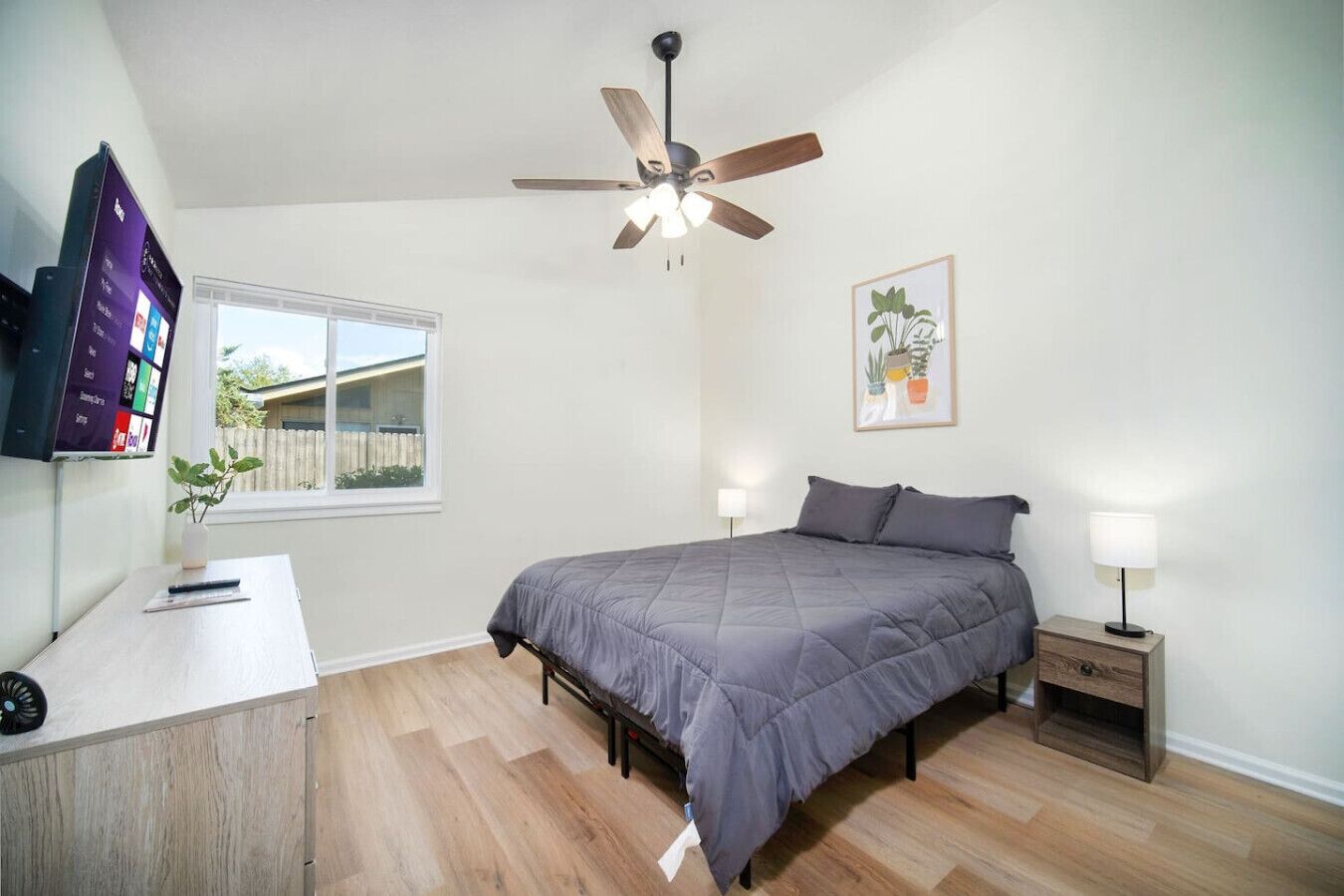 Une chambre à coucher comprenant un lit, des tables de chevet, un ventilateur de plafond, une fenêtre et un téléviseur fixé au mur.