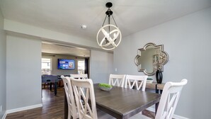 Un comedor con mesa de madera y sillas blancas, una lámpara de araña y un espejo en la pared.
