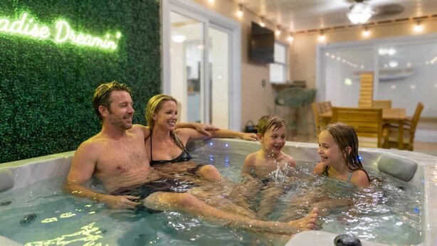 A family in a hot tub with a neon sign in the background. - Private Resort | Pool, Spa, Tiki Bar + Games (Seminole)