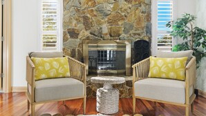 A cozy room with a stone wall, a fireplace, two wicker chairs with patterned cushions, and a small round table. - Private Resort | Pool, Spa, Tiki Bar + Games (Seminole)