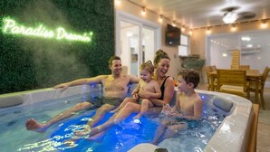 A family enjoying a hot tub with a neon sign reading "Paradise Dreamin'" in the background. - Private Resort | Pool, Spa, Tiki Bar + Games (Seminole)