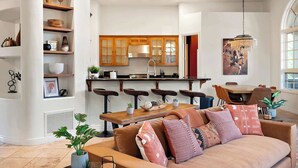 Une cuisine moderne avec des meubles en bois, un coin repas avec une table et des chaises en bois, et un salon avec un canapé et des coussins.