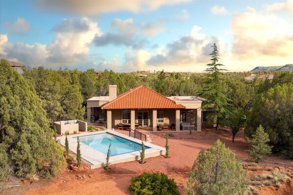 A house with a swimming pool, surrounded by trees and a hilly landscape.