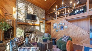 A cozy interior with a stone fireplace, leather sofa, and a wooden ceiling. - 6 Br Cabin~Hot Tub~Fire Pit~Min to Hatley Pointe (Mars Hill)