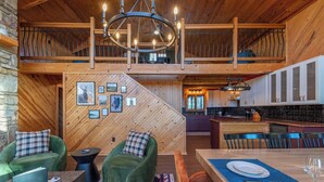 A spacious loft-style room with a dining area, a kitchen, and a staircase leading to an upper level. - 6 Br Cabin~Hot Tub~Fire Pit~Min to Hatley Pointe (Mars Hill)