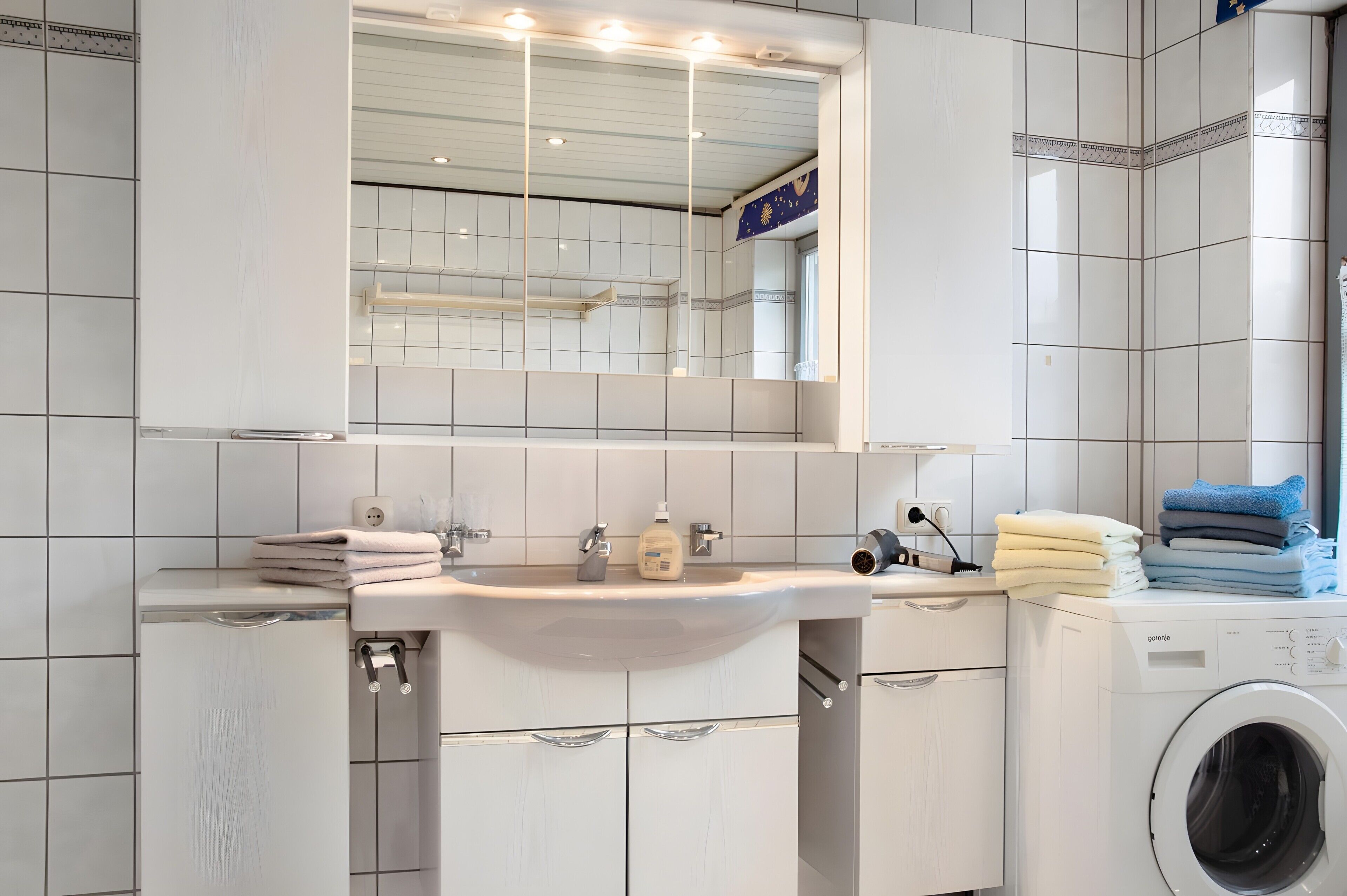 A modern bathroom with a sink, mirror, and washing machine.