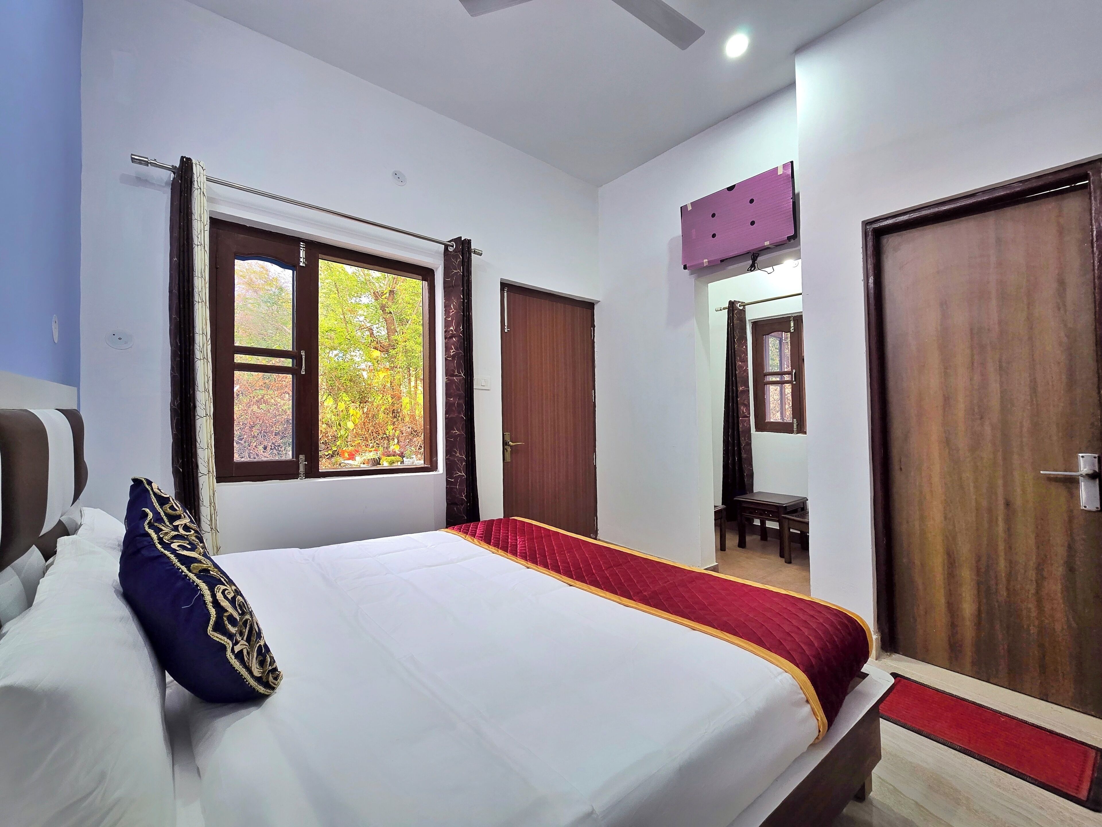 A hotel room with a bed, a window with curtains, a wooden door, and a small table.