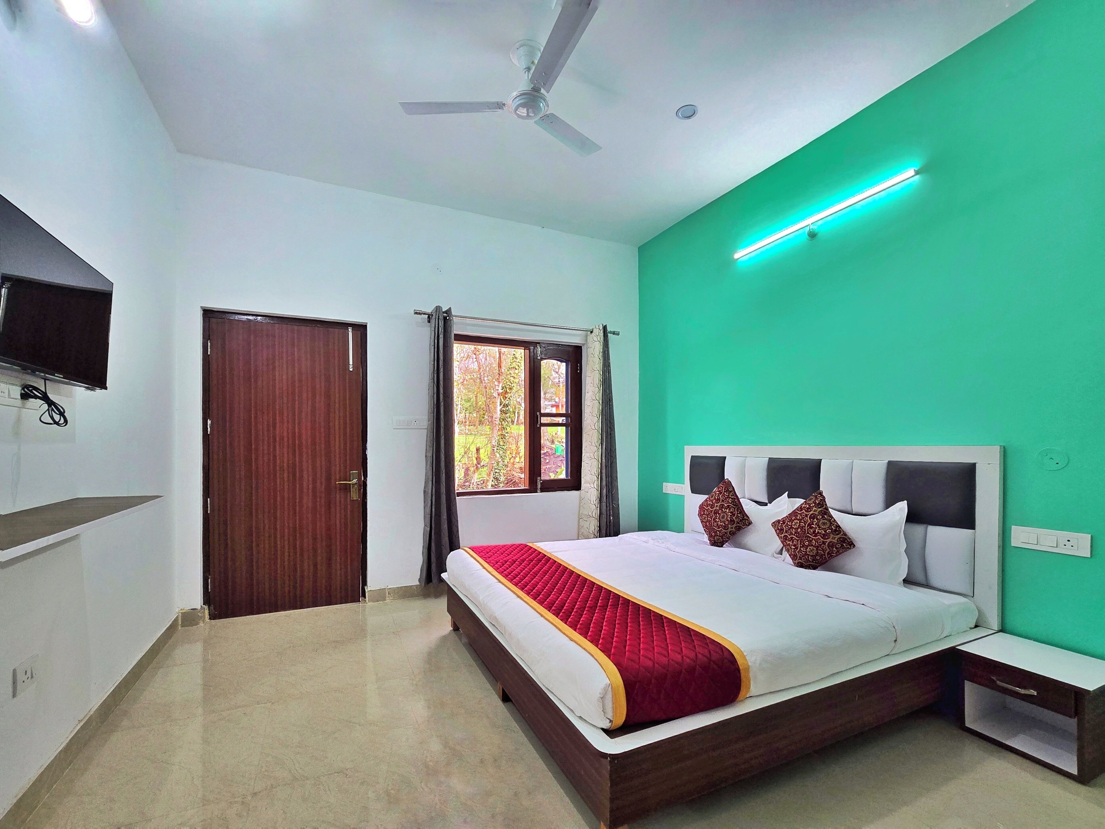 A bedroom with a bed, a ceiling fan, a TV mounted on the wall, and a window with curtains.