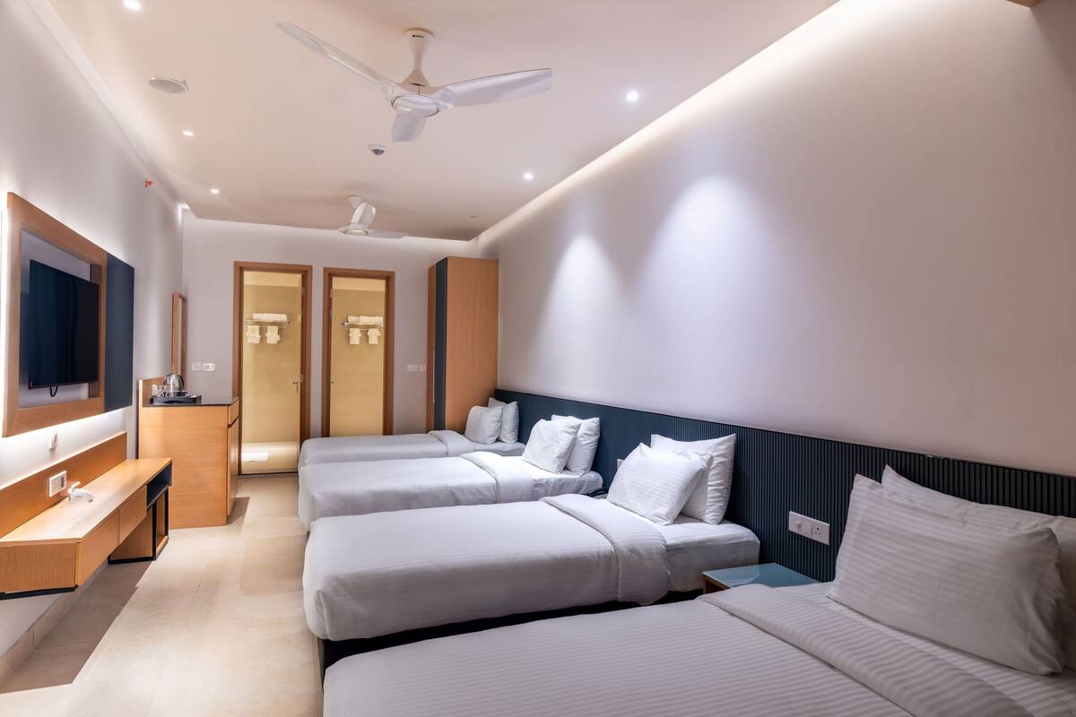 Ein modernes Hotelzimmer mit drei Einzelbetten, einem Schreibtisch, einem Fernseher und einem Deckenventilator.