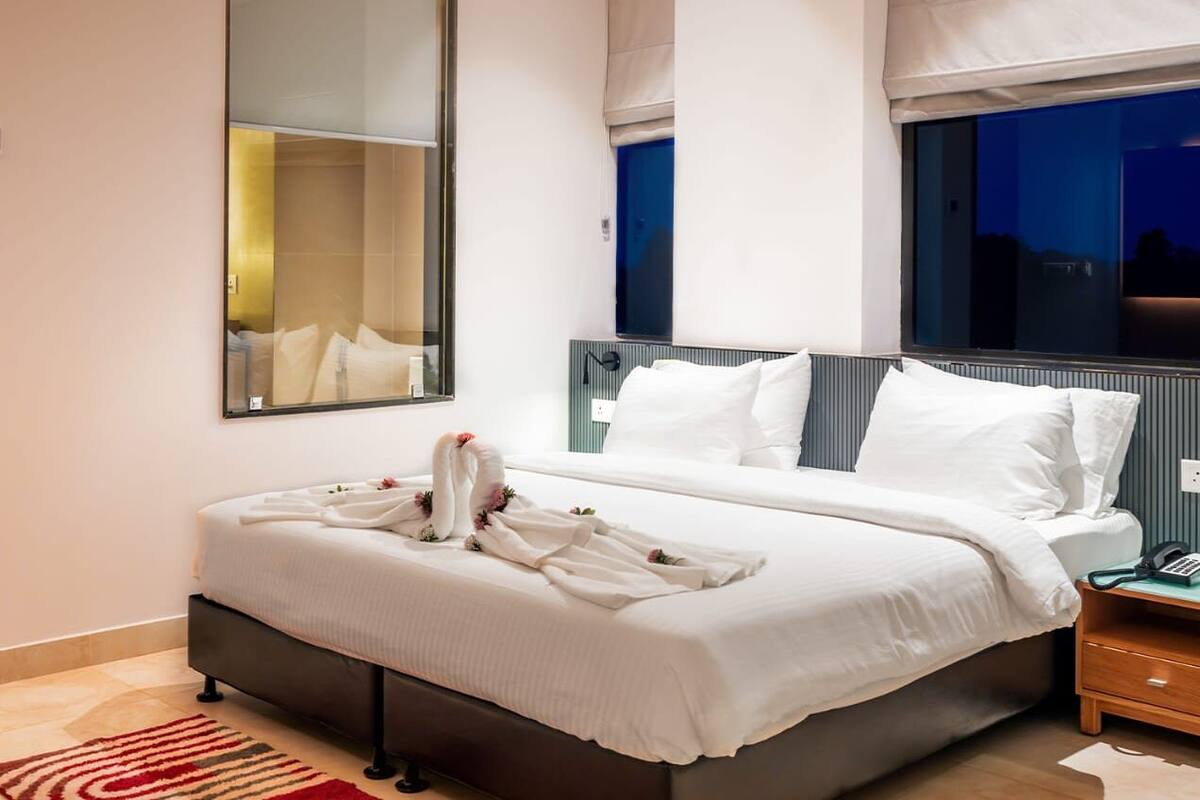 Ein Hotelzimmer mit einem großen Bett, einem Nachttisch mit Lampe und einem großen Spiegel an der Wand.
