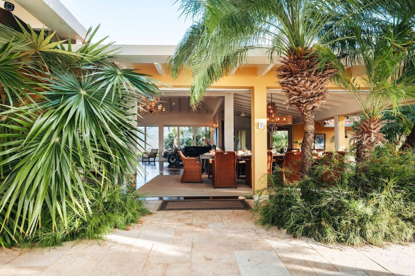 A modern outdoor dining area with a pool, surrounded by lush greenery and palm trees.