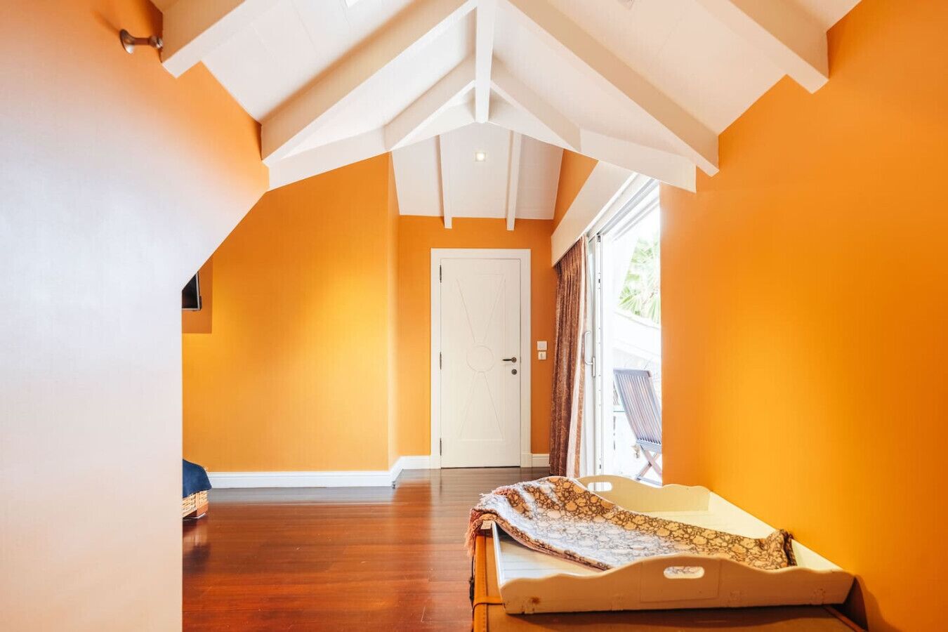 A room with orange walls, a wooden floor, a white door, and a window with curtains.