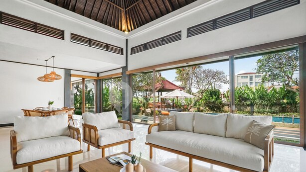 A spacious living area with a large sofa, two armchairs, a wooden coffee table, and a dining table with chairs. Large windows provide a view of the outdoor pool and greenery. - Srimalen Villa by Kozystay - Canggu- (Canggu)