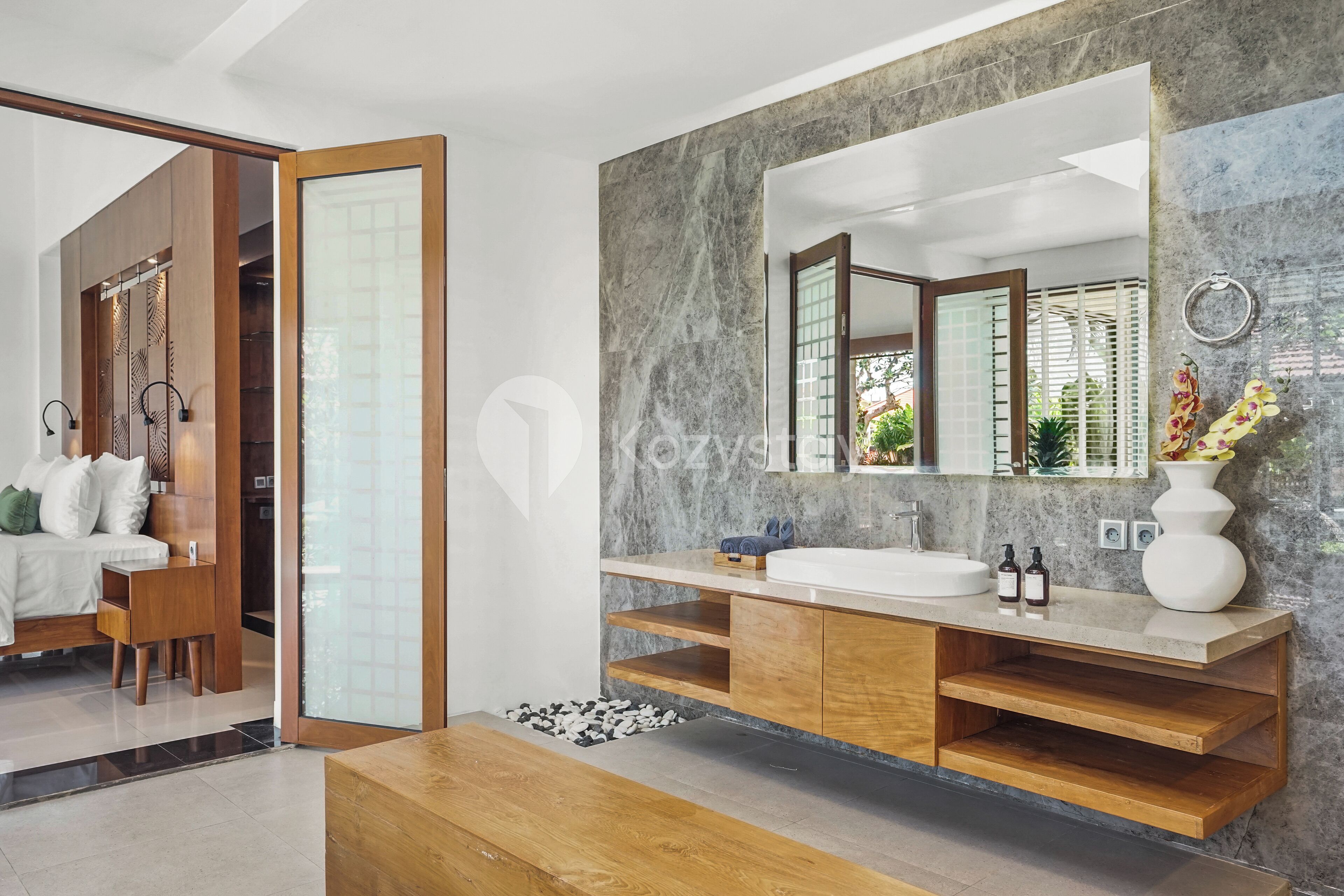 A modern bathroom with a large mirror, wooden vanity, and a marble wall.