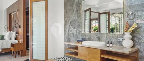 A modern bathroom with a large mirror, wooden vanity, and a marble wall.