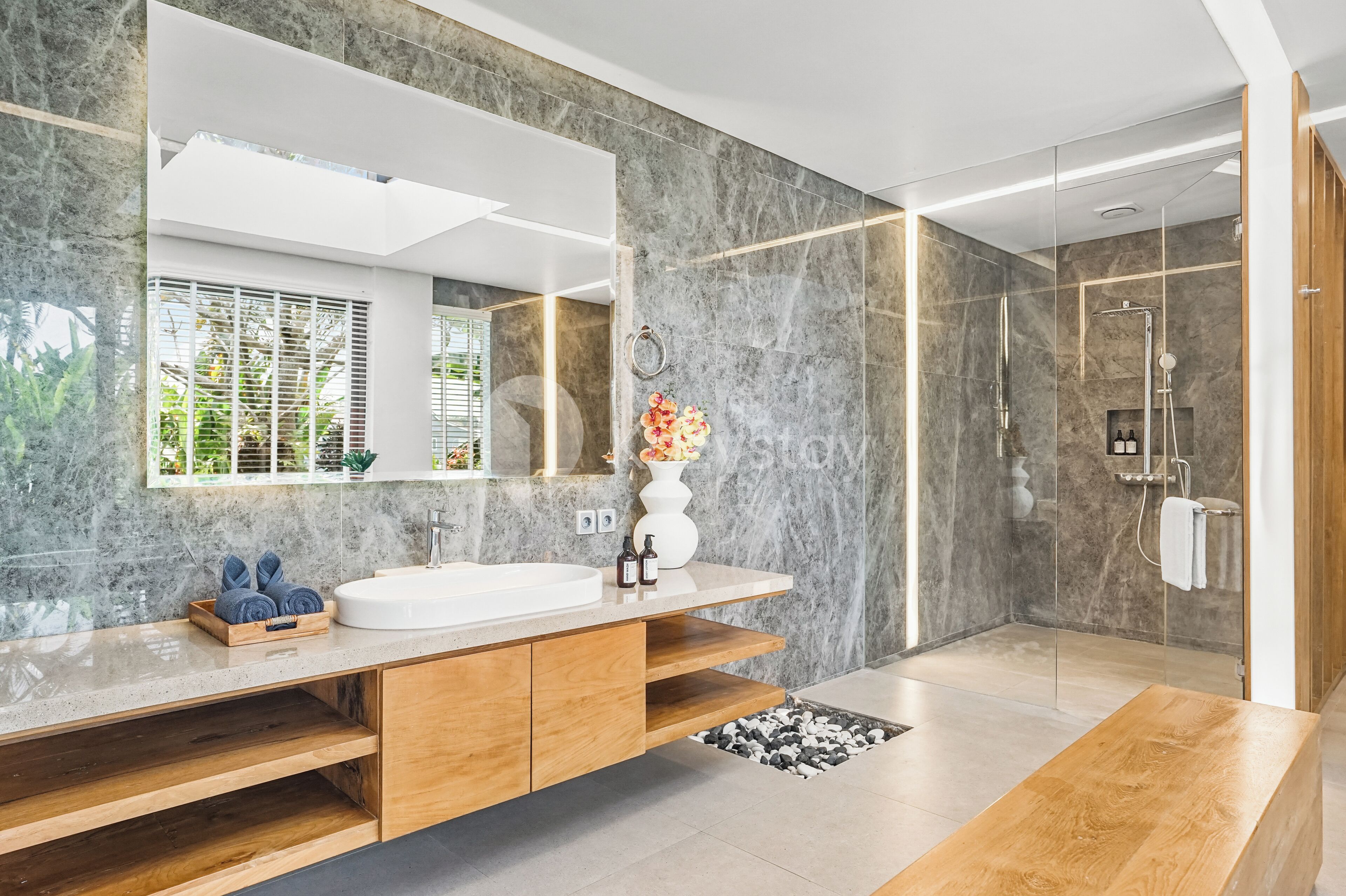 A modern bathroom with a large mirror, marble walls, and a wooden vanity.
