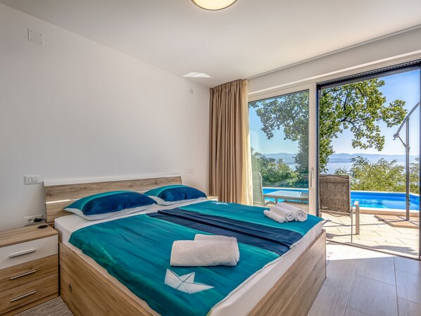 A bedroom with a large bed, a view of a swimming pool, and a door leading to an outdoor area.