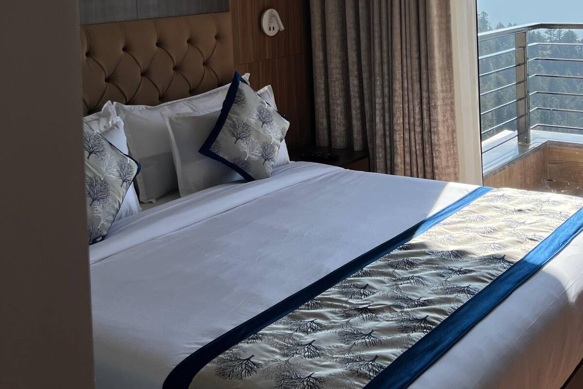 Habitación de hotel con una cama grande, cabecera de madera, vistas a las montañas a través del ventanal y un balcón con barandilla.