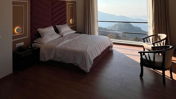 Habitación de hotel moderna con una cama grande, una mesita de noche, una silla y vistas a la montaña a través de la ventana.