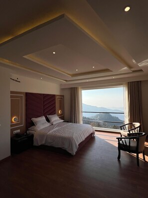 A modern hotel room with a large bed, a nightstand, a chair, and a view of the mountains through the window. - Jot Pass Hotel (Bhattiyat)