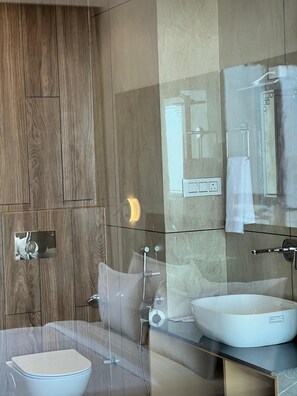 A modern bathroom with a wooden panel wall, a glass shower enclosure, a white sink, and a toilet. - Jot Pass Hotel (Bhattiyat)