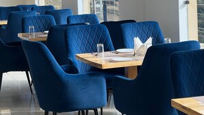Un comedor moderno con sillas tapizadas en azul y mesas, amplias ventanas que ofrecen vistas a un paisaje montañoso.