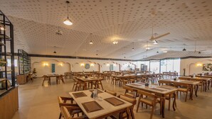 A spacious dining area with multiple tables and chairs, ceiling fans, and pendant lights. - The Rawla Tent Resort & Spa (Garudeshwar)