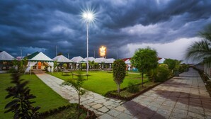 A hotel with multiple white tents, a well-maintained lawn, and a paved walkway. - The Rawla Tent Resort & Spa (Garudeshwar)