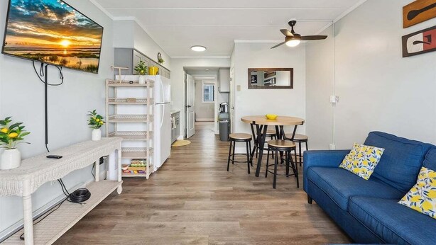 Ein modernes Wohnzimmer mit einem blauen Sofa, einem flachbildfernseher an der Wand, einem Deckenventilator und einem Essbereich mit kleinem Tisch und Stühlen.