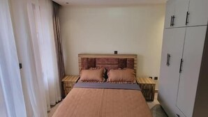 A bedroom with a bed, nightstands, a wardrobe, and a ceiling light. - Legend Hotel (Kigali)