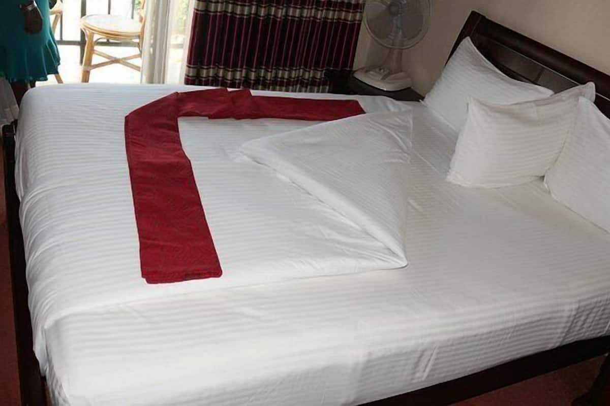 A neatly made bed with white linens and a red accent.