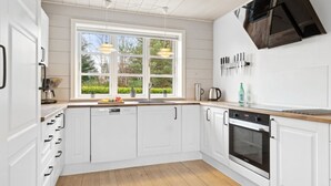Eine moderne Küche mit weißen Schränken, einem eingebauten Backofen und einem großen Fenster, das für natürliches Licht sorgt.