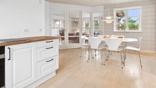Eine moderne Küche mit weißen Schränken und einer Holz Arbeitsplatte, die in einen Essbereich mit weißen Stühlen und einem Tisch übergeht.