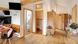 Ein modernes Interieur mit Essbereich, Wandfernseher, Holzbalken und einem sichtbaren Badezimmer.