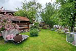 A wooden cabin with a sloped roof, a bench with pillows, a fenced play area, and a small table with chairs. - Apartment 'Waldblick' with Private Garden, Balcony and Wi-Fi (Höslwang)