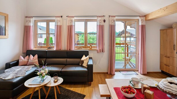 Ein Wohnzimmer mit einer Couch, einem Tisch mit Obstschale und Blick auf einen Balkon.