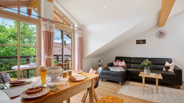 A spacious living area with a dining table, a sofa, and a view of greenery outside. - Apartment 'Neubau - Freundliche' with Mountain View, Shared Garden and Wi-Fi (Höslwang)