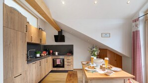 A modern kitchen with wooden cabinets, a dining table with plates and drinks, and a bench. - Apartment 'Neubau - Freundliche' with Mountain View, Shared Garden and Wi-Fi (Höslwang)