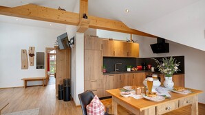 A modern kitchen with wooden cabinets, a dining table with plates, and a bench in a bright room with wooden beams. - Apartment 'Neubau - Freundliche' with Mountain View, Shared Garden and Wi-Fi (Höslwang)
